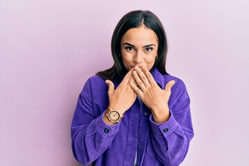 Young brunette woman wearing casual clothes laughing and embarrassed giggle covering mouth with...
