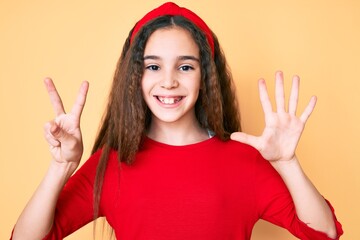 Cute hispanic child girl wearing casual clothes and diadem showing and pointing up with fingers number seven while smiling confident and happy.