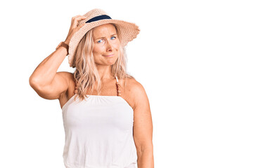 Middle age fit blonde woman wearing summer hat confuse and wonder about question. uncertain with doubt, thinking with hand on head. pensive concept.