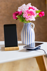 a phone charging on a wireless charger. Standing on the table in the apartment next to the vase of flowers
