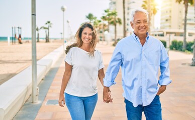Obraz premium Middle age hispanic couple smiling happy walking at the beach.