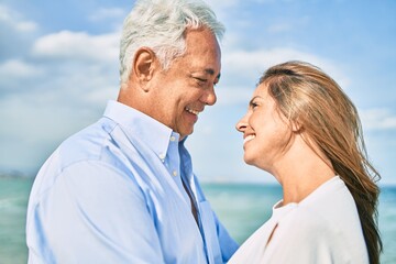 Middle age hispanic couple smiling happy and hugging walking at the beach