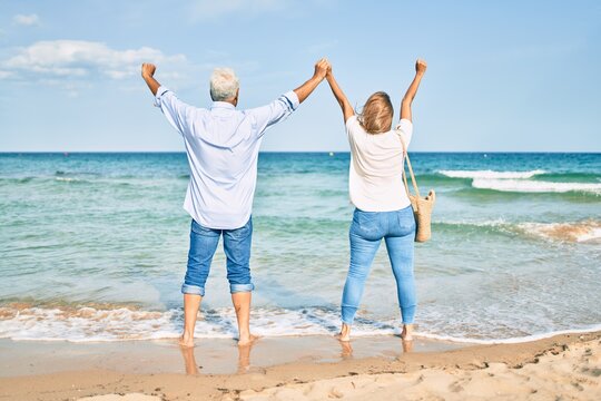 Middle age hispanic couple breathing with arms raised at the beach.
