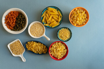 pasta in ceramic bowl. penne, farfalle tonde, butterfly, auger, couscous, colorful pasta, barley noodle, kesme, turkish noodle, erişte, ditalini type of pasta on blue background. orange white red.