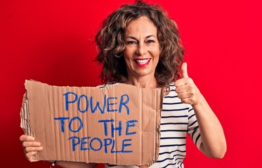 Senior woman asking for social movement holding banner with power to the people message smiling happy and positive, thumb up doing excellent and approval sign