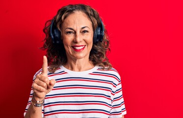 Middle age brunette woman listening to music using headphones over red background smiling with an...