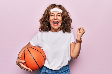 Middle age brunette basketball player woman holding game ball over isolated pink background screaming proud, celebrating victory and success very excited with raised arm - Powered by Adobe