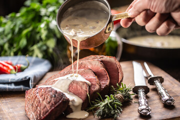 Rump steak cut to slices on a chopping board next to a knife and rosemary, with a mushroom sauce...