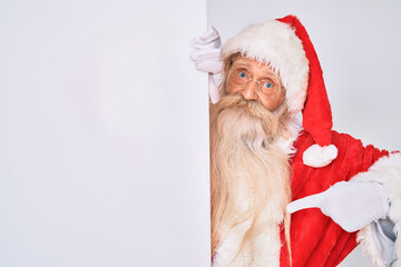 Old senior man with grey hair and long beard wearing santa claus costume holding banner pointing finger to one self smiling happy and proud