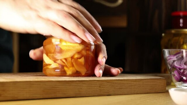 Woman's hand opening preserving jar with apple jam in the kitchen.