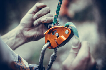 Man's hands operating a rock climbing belaying device - obrazy, fototapety, plakaty