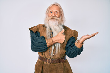 Old senior man with grey hair and long beard wearing viking traditional costume showing palm hand and doing ok gesture with thumbs up, smiling happy and cheerful