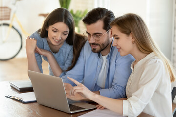Smiling young diverse colleagues sit at desk look at laptop brainstorm discuss financial project together. Millennial coworkers employees work cooperate on computer in office. Teamwork concept.