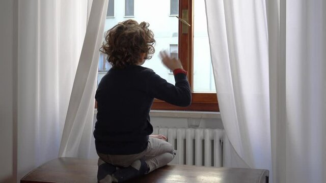 Europe, Italy , Milan -  children boy  six years  at home during quarantine  due covid-19 Coronavirus outbreak - lifestyle in apartment - look and say hello from the window 