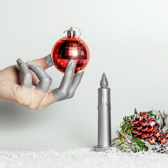 hand in silver color holding red christmas ball on gray background with christmas ornament