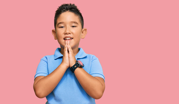 Little boy hispanic kid wearing casual clothes praying with hands together asking for forgiveness smiling confident.