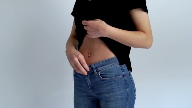 Young woman is showing her belly button or navel piercing isolated on white background.