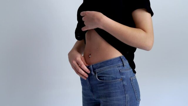 Young woman is showing her belly button or navel piercing isolated on white background.
