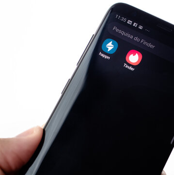 Happn e Tinder,  aplicativos de relacionamento. Uma pessoa mostrando o celular com os apps Happn e Tinder na tela. 