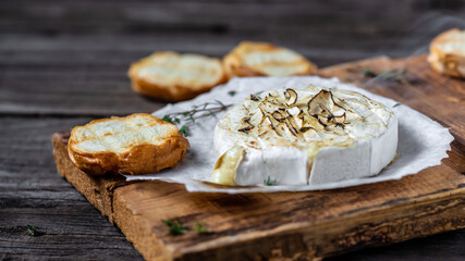 Delicious hot baked camembert with thyme and baguette bread on wooden table