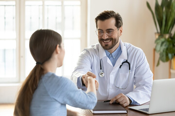 Smiling male GP shake hand of female patient at consultation in clinic get acquainted at meeting....