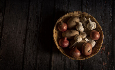 onion, potato and garlic vegetable in basket on dark wooden background