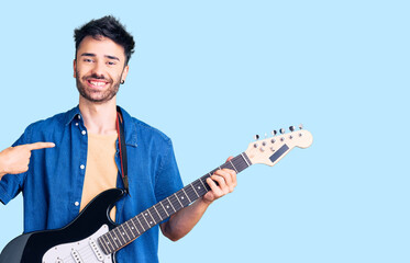 Young hispanic man playing electric guitar pointing finger to one self smiling happy and proud