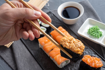 a variety of Japanese rolls and sushi on a textured black plate. Side view. Bamboo sticks hold one gunkan. Close up