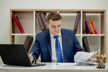 Young businessman working with documents looking through papers in folder, sitting at office desk