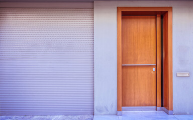 Contemporary house, pale grey facade and natural wood entrance door by the sidewalk with space for your text