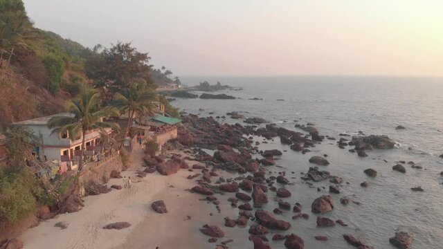 Rocky ocean coast and old buildings in Arambol Beach at sunset in Goa, India - Aerial Fly-over shot