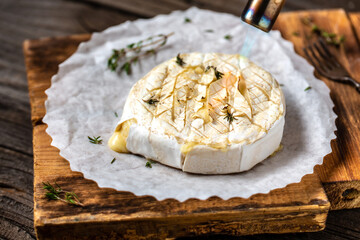 Delicious hot baked camembert with thyme and baguette bread on wooden table