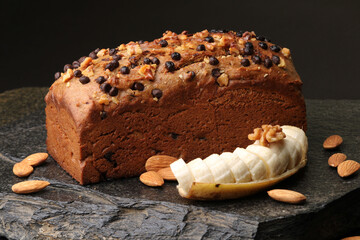 Homemade banana bread with walnut, almonds on a stone background.