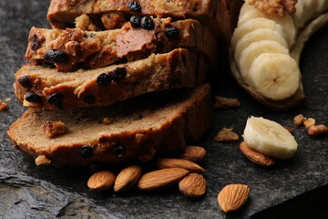 Loaf of banana bread on Dark stone background. with almonds and walnut