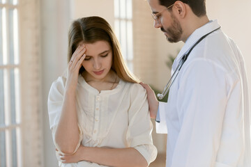 Fototapeta premium Caring young Caucasian male doctor support comfort unhappy distressed female patient hearing bad news in hospital. Supportive man GP or physician touch show empathy to sad woman client in clinic.