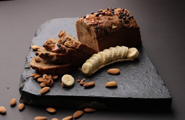 Loaf of banana bread on Dark stone background. with almonds and walnut