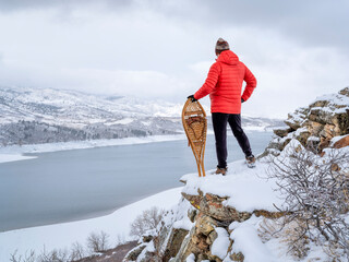 man with classic Huron snowshoes is overlooking a mountain lake in winter scenery - Horsetooth Reservoir in northern Colorado