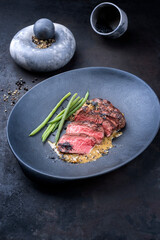 Modern Style gebratenes dry aged Wagyu Roastbeef Pfeffersteak mit grünen mini Bohnen in Pfeffer Sauce serviert als close-up in einem Design Teller