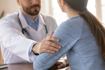 Crop close up of male doctor in white medical uniform touch female patient arm show empathy care at...