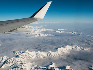 Aerial view of the Italian Swiss Alps in winter, with generic aeroplane wing. Snowcapped mountain range and glaciers. Expansive view, clear blue sky.