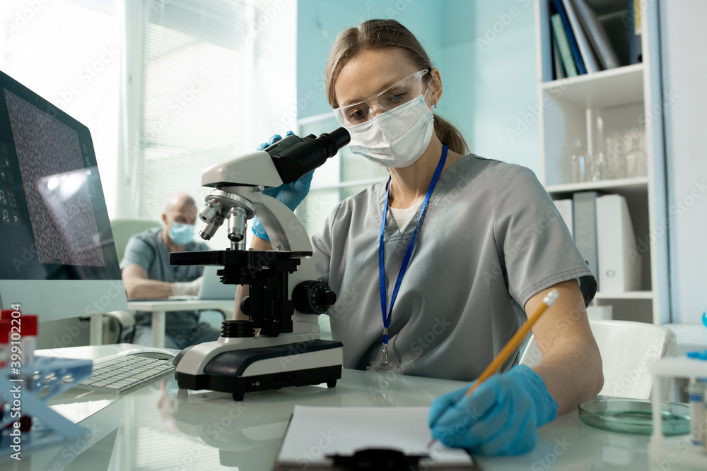 Aufkleber Female laboratory worker making notes in document while working with microscope