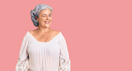 Senior woman with gray hair wearing bohemian style winking looking at the camera with sexy expression, cheerful and happy face.