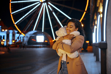 Happy woman hugs soft toy in night amusement park