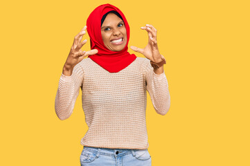 Young african american woman wearing traditional islamic hijab scarf shouting frustrated with rage,...