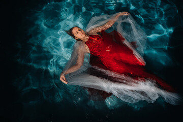 Fototapeta na wymiar A girl in a red dress is floating on the water.A journey on the water of a single woman