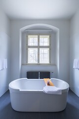 Naklejka na ściany i meble Comfortable white bathtub and sink standing in modern bathroom with white walls and concrete floor. Interior with spectacular oval bath. 