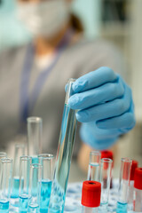 Gloved hand of clinician taking flask with sample of vaccine before testing it