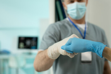 Gloved hands of two clinicians in protective workwear making punch bump