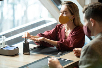 Fototapeta premium Young blond female in smart casualwear and protective mask taking sanitizer