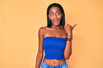 Young african american woman wearing casual clothes smiling with happy face looking and pointing to the side with thumb up.